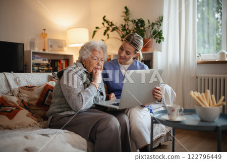 Social worker helping elderly lady with managing her finances, teaching her to use online banking on laptop. 122796449