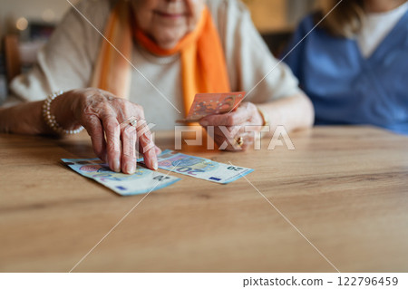 Social worker helping elderly lady with managing her finances, counting banknotes. 122796459