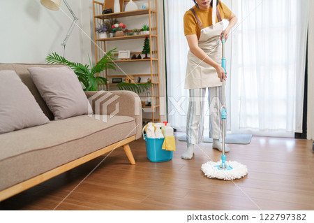 Asian housemaid scrubbing the wooden floor in a modern living room with cleaning supplies 122797382