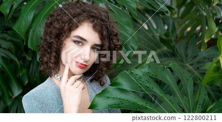 Woman with curly hair is standing in front of a green plant 122800211
