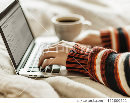 A cozy work-from-home scene with hands typing on a laptop and a cup 122800321