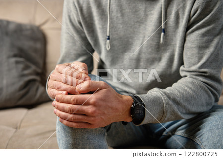 Man holding knee in pain while sitting on couch 122800725
