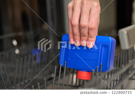 Hand placing dishwasher cleaner bottle inside empty dishwasher 122800735