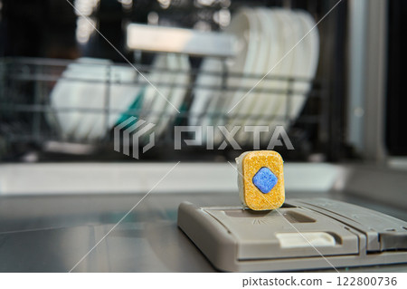 Dishwasher detergent tablet on dispenser with clean dishes in background 122800736