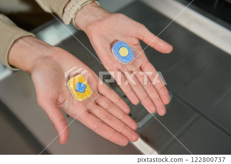 Dishwasher detergent tablets comparison in hands near open dishwasher 122800737