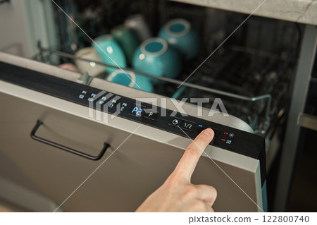 Finger pressing button on dishwasher control panel 122800740