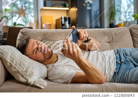 Man relaxing on sofa using smartphone at home 122800843