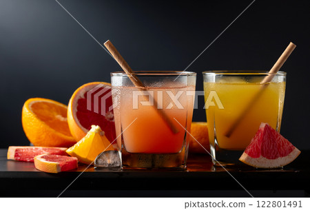 Glasses of grapefruit and orange juice with ice on a black background. Glasses of grapefruit and orange juice with ice on a black background. 122801491
