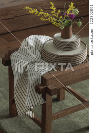 Set of ceramic dinnerware on rattan stool, linen tea towel,  wild spring flowers. Home decoration concept 122802091
