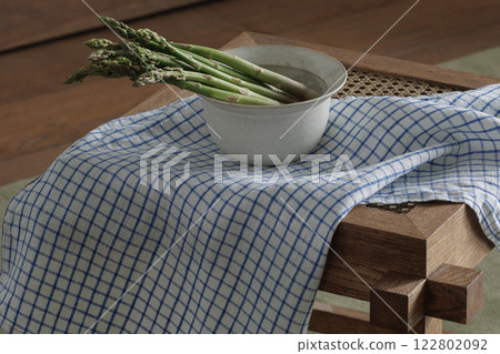 Fresh asparagus in ceramic bowl on rattan stool with linen tea towel. Healthy lifestyle concept 122802092