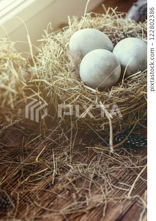 Atmospheric Easter set. Three symbolic blue eggs in birds nest among hay on windowsill, vertical image. 122802386