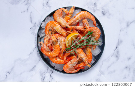 Freshly frozen shrimp on ice, with lemon and rosemary, on the marble table, top view, no people 122803067