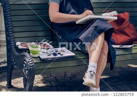 An unrecognizable female artist sits on a bench and creates another masterpiece on canvas. With space to copy. High quality photo An unrecognizable female artist sits on a bench and creates another masterpiece on canvas. With space to copy. High quality photo 122803759