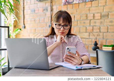 Portrait off middle-aged business woman working with laptop, using phone, sitting at desk Portrait off middle-aged business woman working with laptop, using phone, sitting at desk 122804121