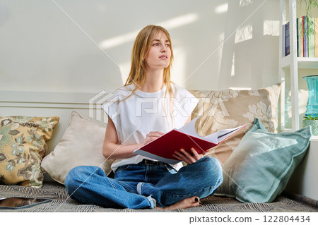Portrait of female student sitting on couch with notebook, studying at home Portrait of female student sitting on couch with notebook, studying at home 122804434