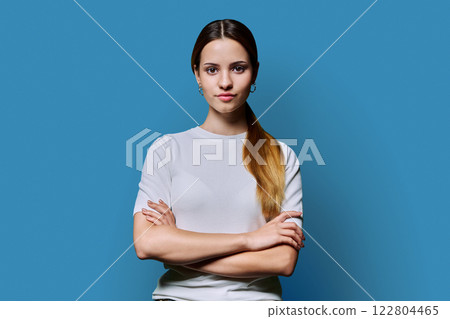 Beautiful young girl with crossed arms looking at camera on blue background 122804465