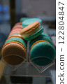 Close-up of colorful macarons with white cream filling displayed under soft lighting on a countertop with a blurred background and selective focus highlighting their delicate texture and vibrant hues 122804847