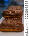 A delicious gourmet eclair filled with creamy custard, topped with crunchy peanuts, rich chocolate glaze, and a luxurious golden sprinkle, creating a visually appealing and indulgent dessert. 122804848