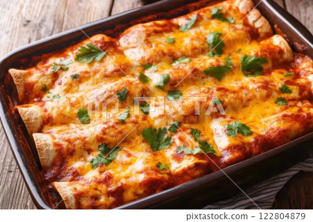 Baked enchiladas with melted cheese, rich sauce, and fresh cilantro in a rustic tray. A classic Mexican dish 122804879