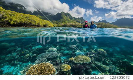 Two snorkelers explore a vibrant coral reef in crystal clear waters, with lush mountains in the background 122805072