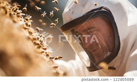 A beekeeper in protective gear examines a hive, surrounded by buzzing bees in the golden light 122805089