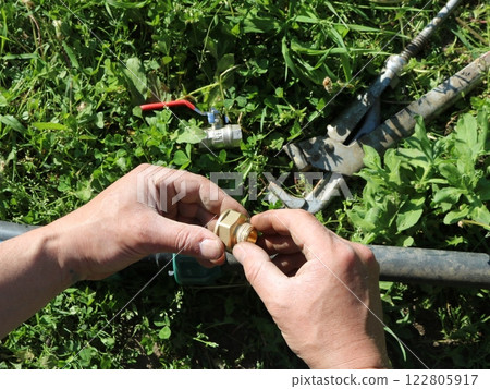 male hands making connection of parts in garden irrigation structure, close-up, adjustment of garden water supply system running on green lawn 122805917