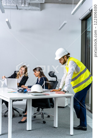 Male engineer in a yellow vest and card cap working in the office Male engineer in a yellow vest and card cap working in the office 122806880