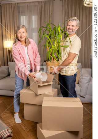 Senior couple moving house packing boxes with belongings together in their home Senior couple moving house packing boxes with belongings together in their home 122806907