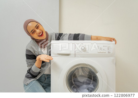 A Happy Woman Enthusiastically Showcasing Her Brand New Washing Machine at Home 122806977