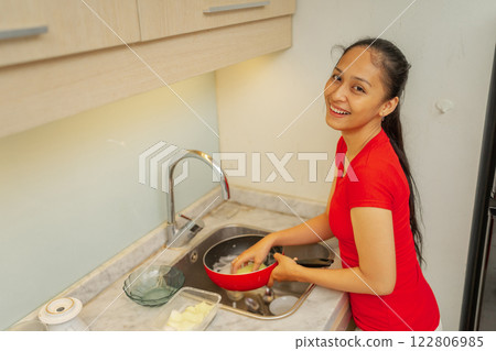 A Woman is Joyfully Washing Dishes in a Bright and Cheerful Kitchen Space 122806985