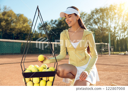 Caucasian female exercising outdoors training with tennis balls on sunny tennis court Caucasian female exercising outdoors training with tennis balls on sunny tennis court 122807008