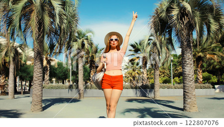 Cheerful young woman in summer park wearing backpack on palm trees background 122807076