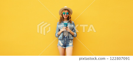 Summer portrait of happy young woman with mobile phone looking at device on yellow background 122807091