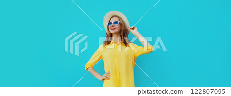 Beautiful young woman posing wearing summer straw hat, yellow shirt on blue studio background 122807095