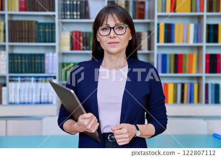 Portrait of middle aged serious woman teacher professor with laptop inside library 122807112