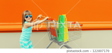 Happy little girl child walking with trolley cart and colorful shopping bags on city street Happy little girl child walking with trolley cart and colorful shopping bags on city street 122807170
