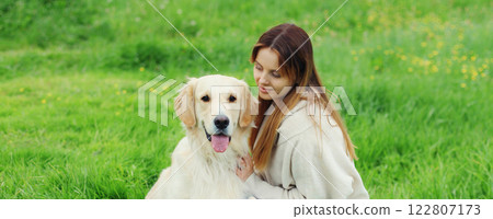 Happy owner young woman with Golden Retriever dog sitting on grass together in summer park 122807173