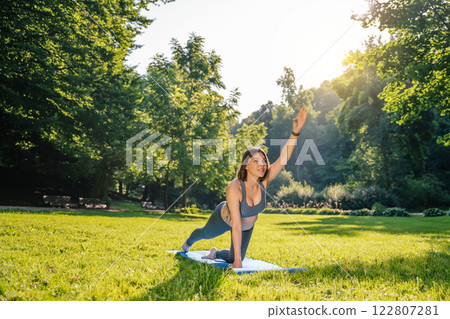 Young pregnant woman doing stretching exercises in the park on a green lawn 122807281