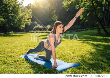 Young pregnant woman doing stretching exercises in the park on a green lawn 122807282