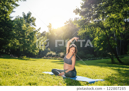 Young pregnant woman doing stretching exercises in the park on a green lawn 122807285