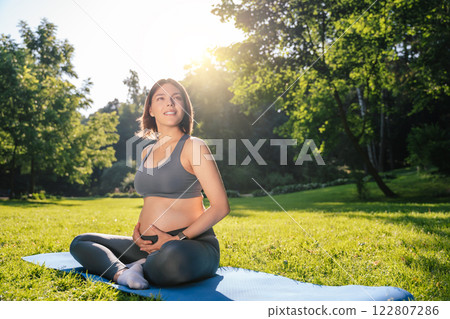 Young pregnant woman doing stretching exercises in the park on a green lawn 122807286