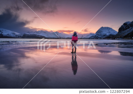 Woman on the arctic sandy beach, snowy mountains and red sky Woman on the arctic sandy beach, snowy mountains and red sky 122807294