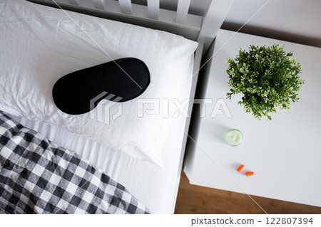 Cozy bedroom scene with sleep mask, cushions, and nightstand decor Cozy bedroom scene with sleep mask, cushions, and nightstand decor 122807394