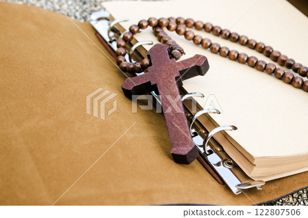A simple wooden cross lies on an open brown notebook, signifying humility, faith, and a connection to spirituality. This evokes thoughts of prayer, scripture study, and religious dedication. 122807506