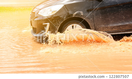 A vehicle navigates through muddy floodwater, depicting urban resilience and the impact of heavy rain. This image highlights extreme weather, climate change, and transportation challenges. 122807507