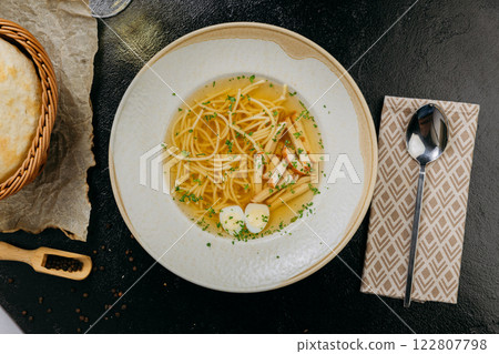 Clear broth soup with noodles, mushrooms, quail eggs, and herbs, served in an gourmet presentation 122807798