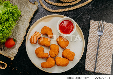 Crispy chicken nuggets with ketchup on plate with fresh ingredients in stylish food presentation 122807803