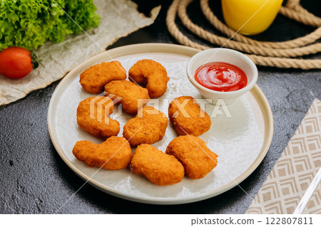 Crispy chicken nuggets with ketchup on plate with fresh ingredients in stylish food presentation 122807811