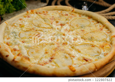 Gourmet pear and blue cheese pizza with pine nuts on wooden board in stylish restaurant setting Gourmet pear and blue cheese pizza with pine nuts on wooden board in stylish restaurant setting 122807822
