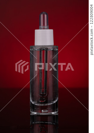 Transparent Glass Dropper Bottle with Liquid on Red Background Transparent Glass Dropper Bottle with Liquid on Red Background 122809004